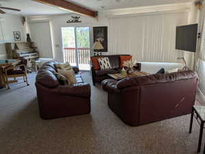 Living area featuring sliding glass doors to the exterior deck, white vertical blinds, and exposed wood beam accents