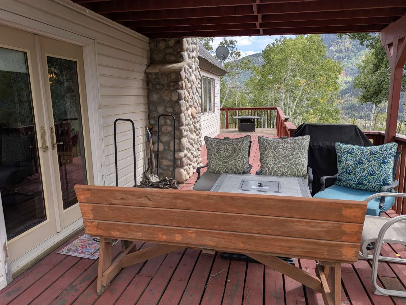 Expansive red-stained deck featuring a stone-clad exterior wall and glass-paneled double doors