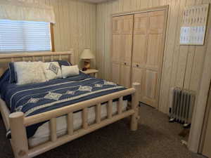 Wood-paneled interior walls, window with blinds, bi-fold closet doors, and carpet flooring