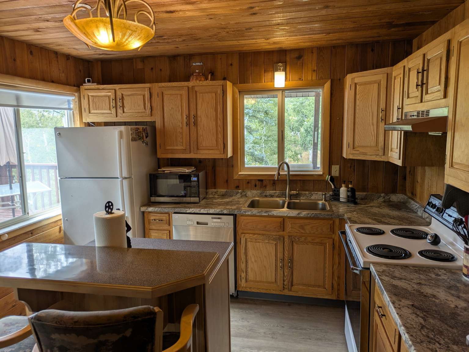 Kitchen featuring wood plank walls and ceiling, light wood-finish cabinetry, speckled countertops, and a double basin stainless steel sink with a gooseneck faucet