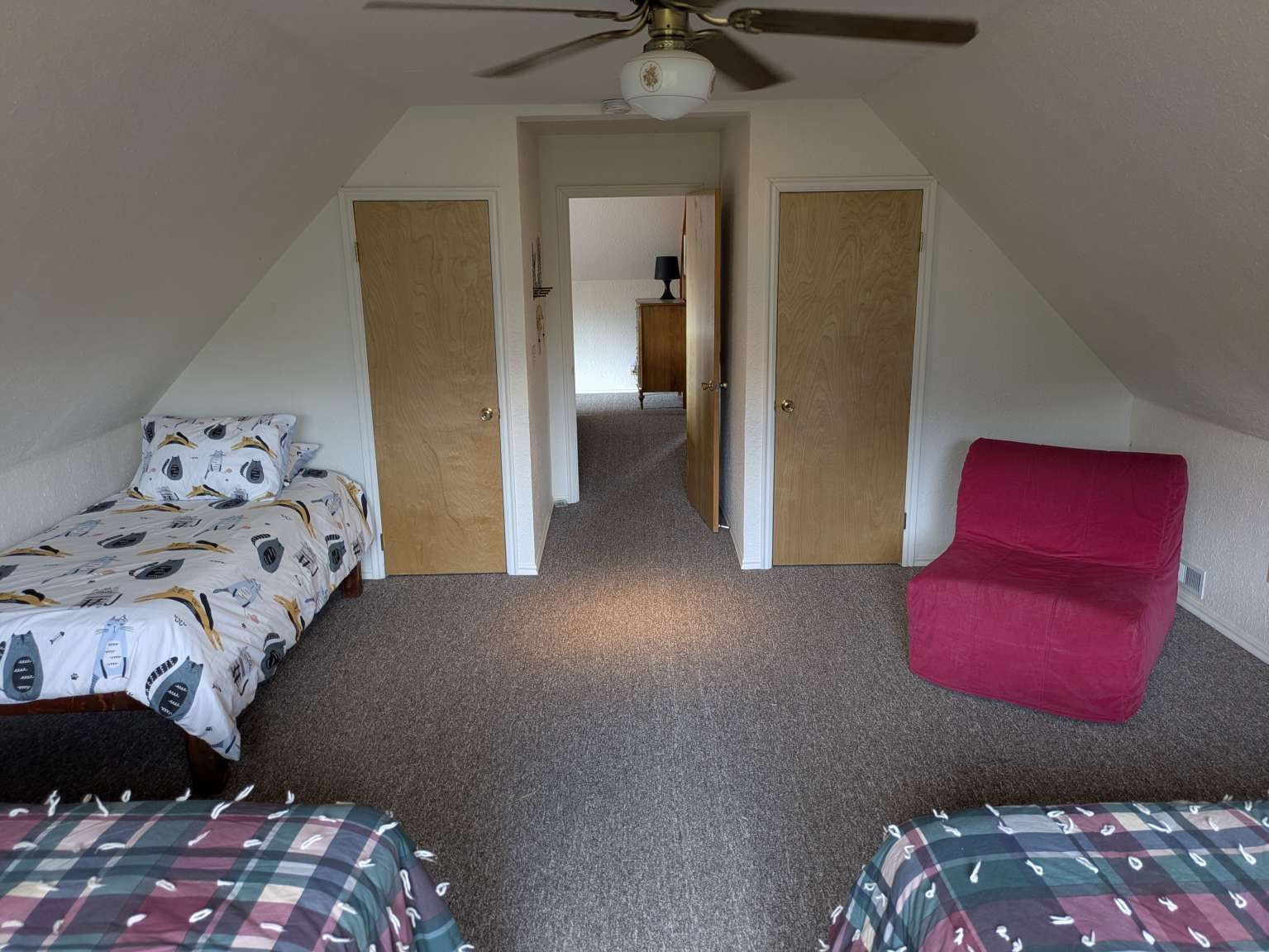 Carpeted room featuring an angled ceiling, a ceiling fan with integrated lighting, two light wood-finish doors, and a doorway leading to an additional space