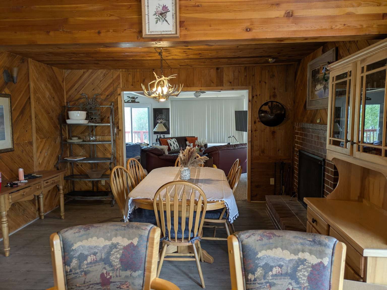 Dining area featuring wood-paneled walls, wood-finish flooring, and a fireplace with a brick surround