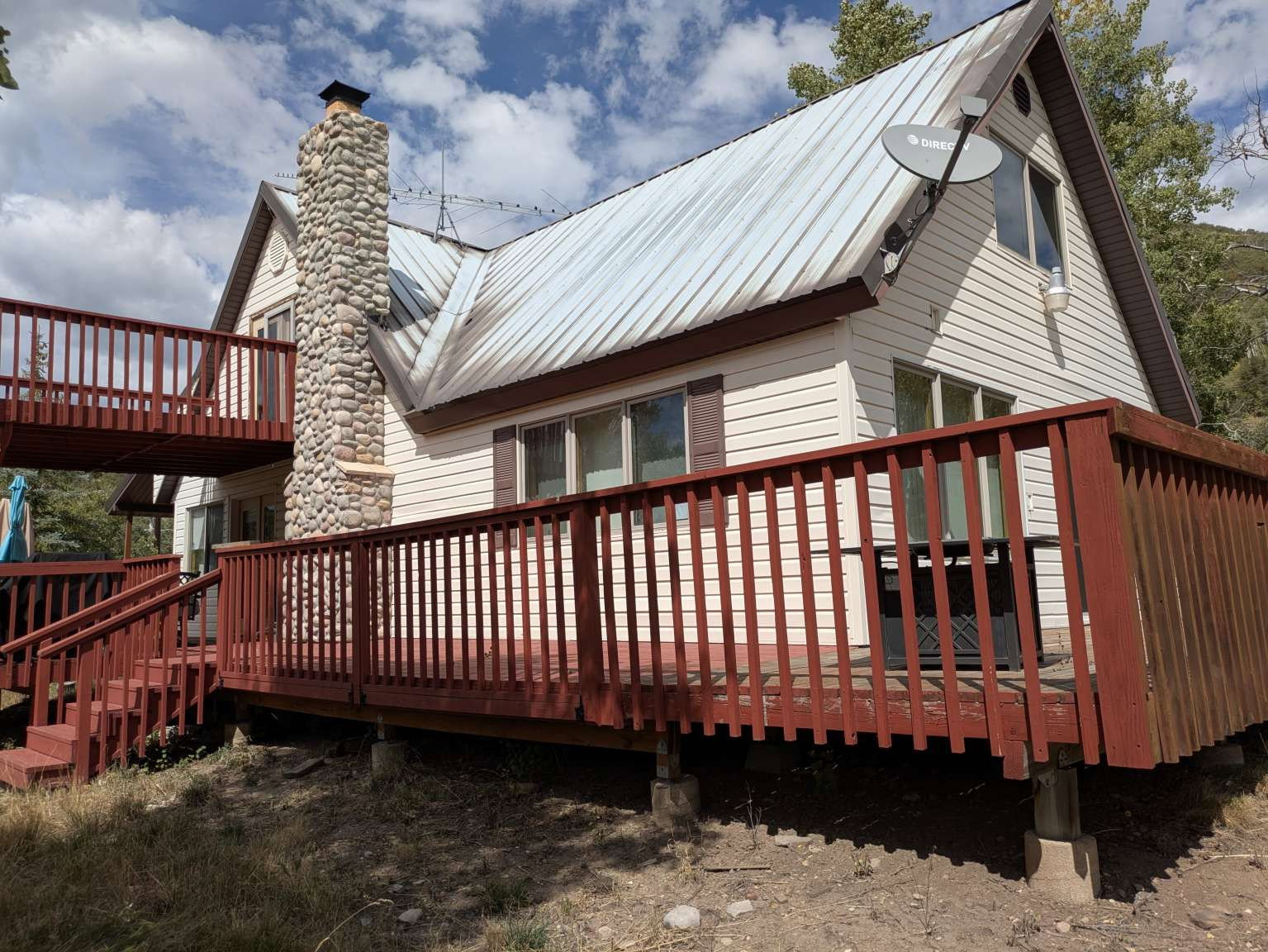 Two-story exterior with light-colored siding, a metal roof, and a prominent stone chimney