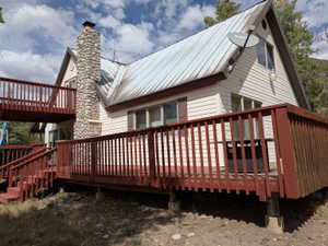 Two-story exterior with light-colored siding, a metal roof, and a prominent stone chimney