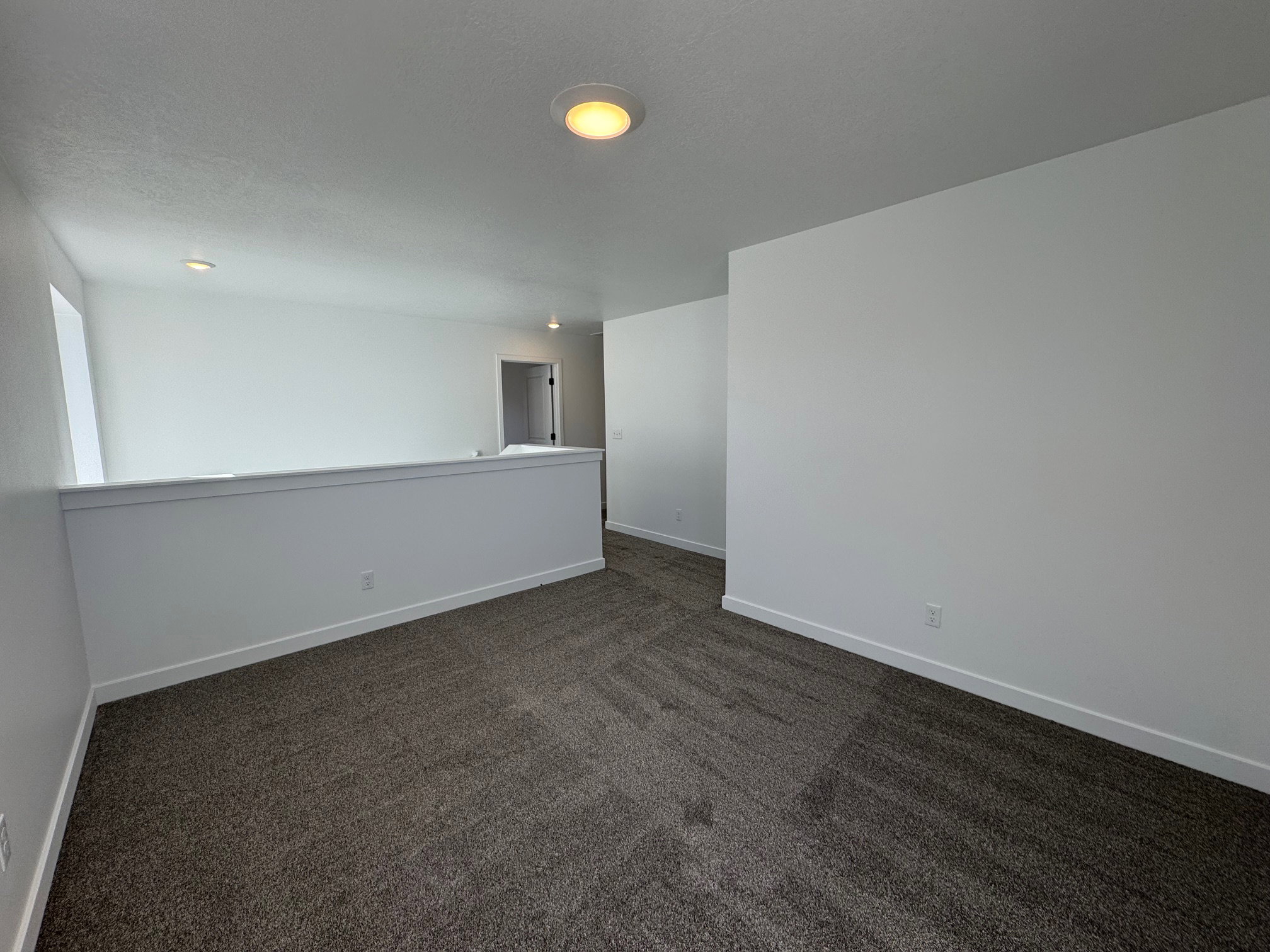 Spacious upper-level loft area with neutral carpeting and recessed lighting