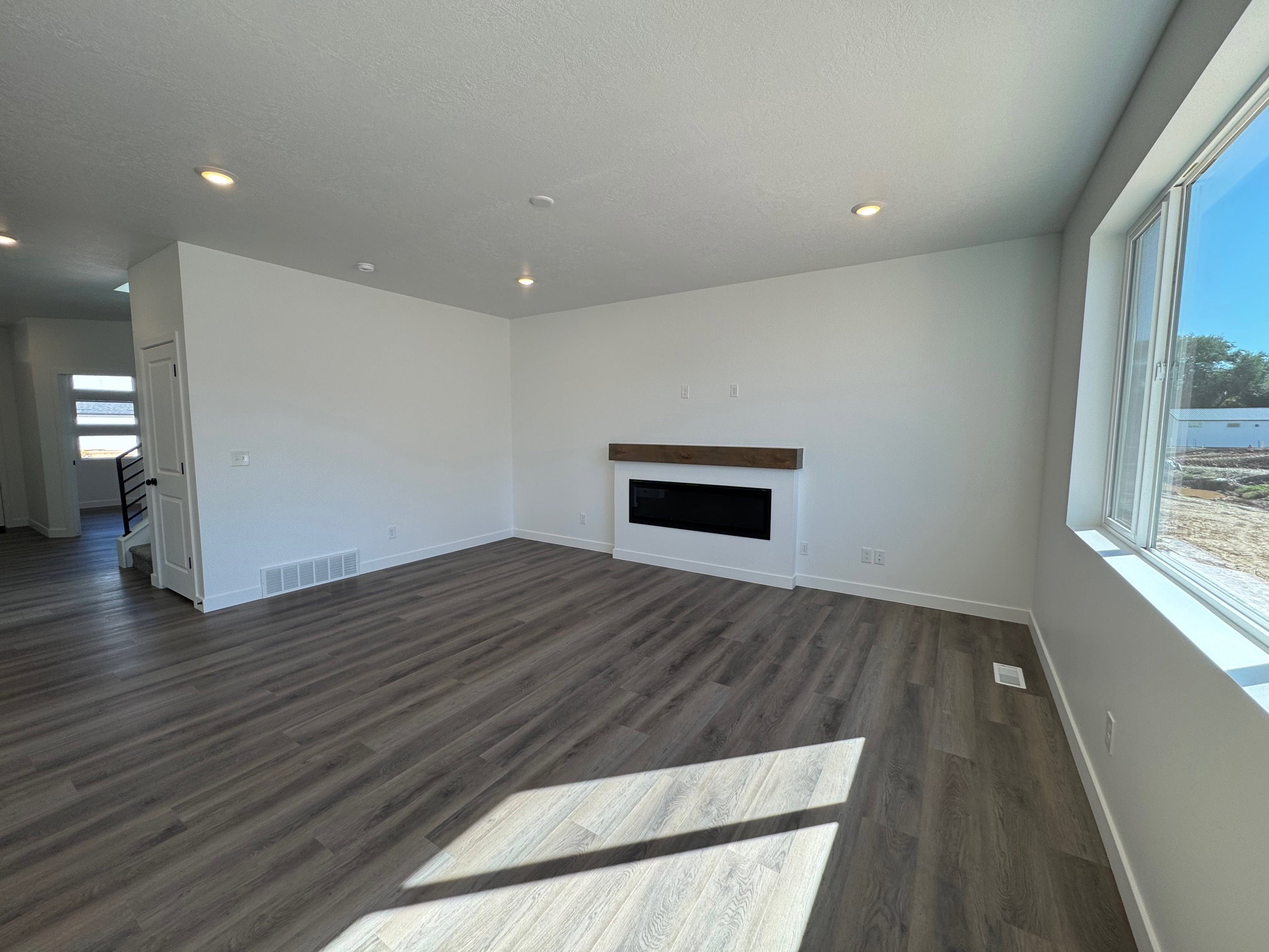 Spacious room featuring wood-finish flooring, recessed lighting, and a contemporary linear fireplace with a wood mantle