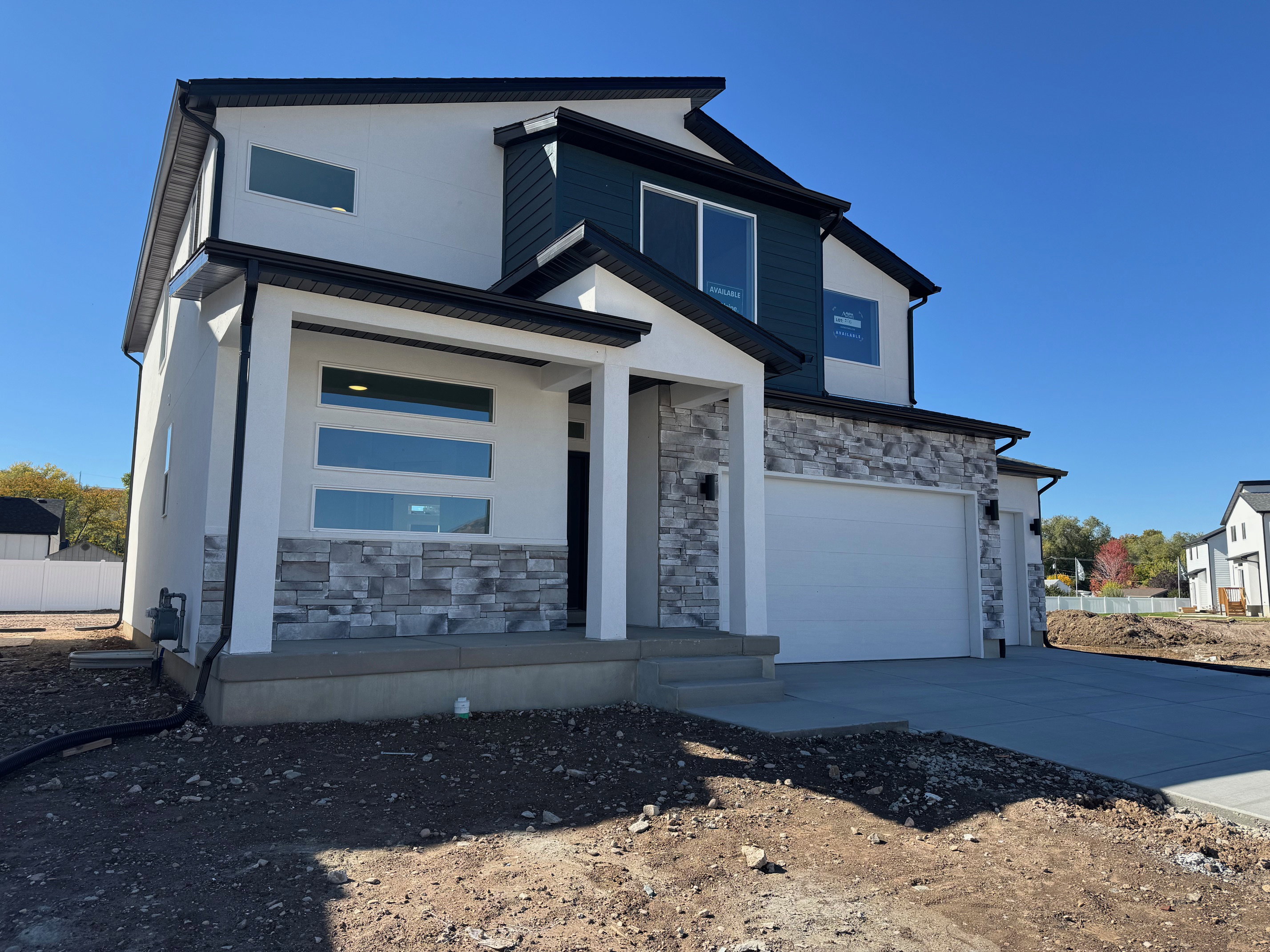Contemporary exterior featuring white stucco, stacked stone accents, dark blue siding, black-framed windows, and a two-car garage