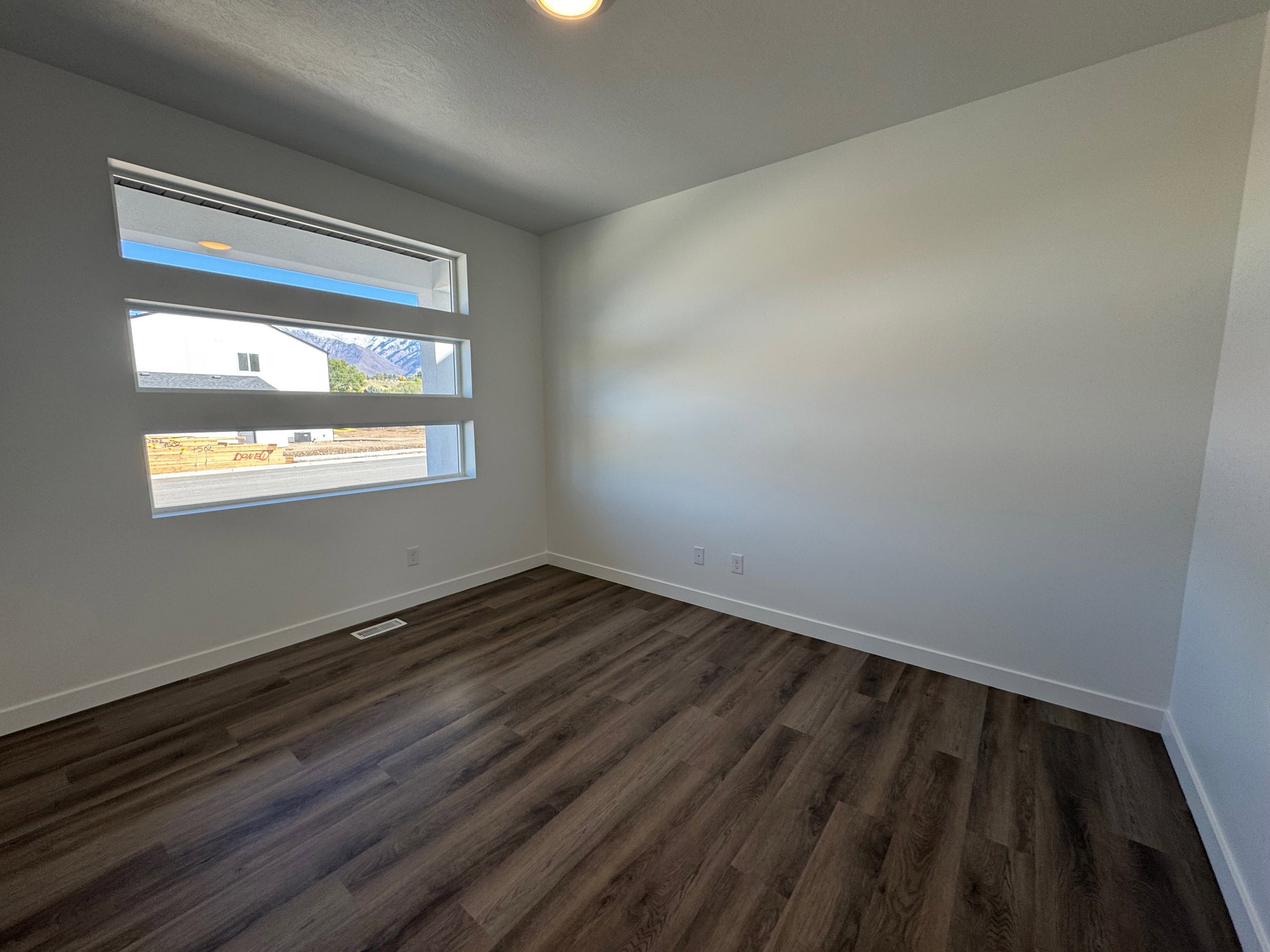 Light-filled room featuring a horizontal window design, wood-finish flooring, white baseboards, and neutral wall tones