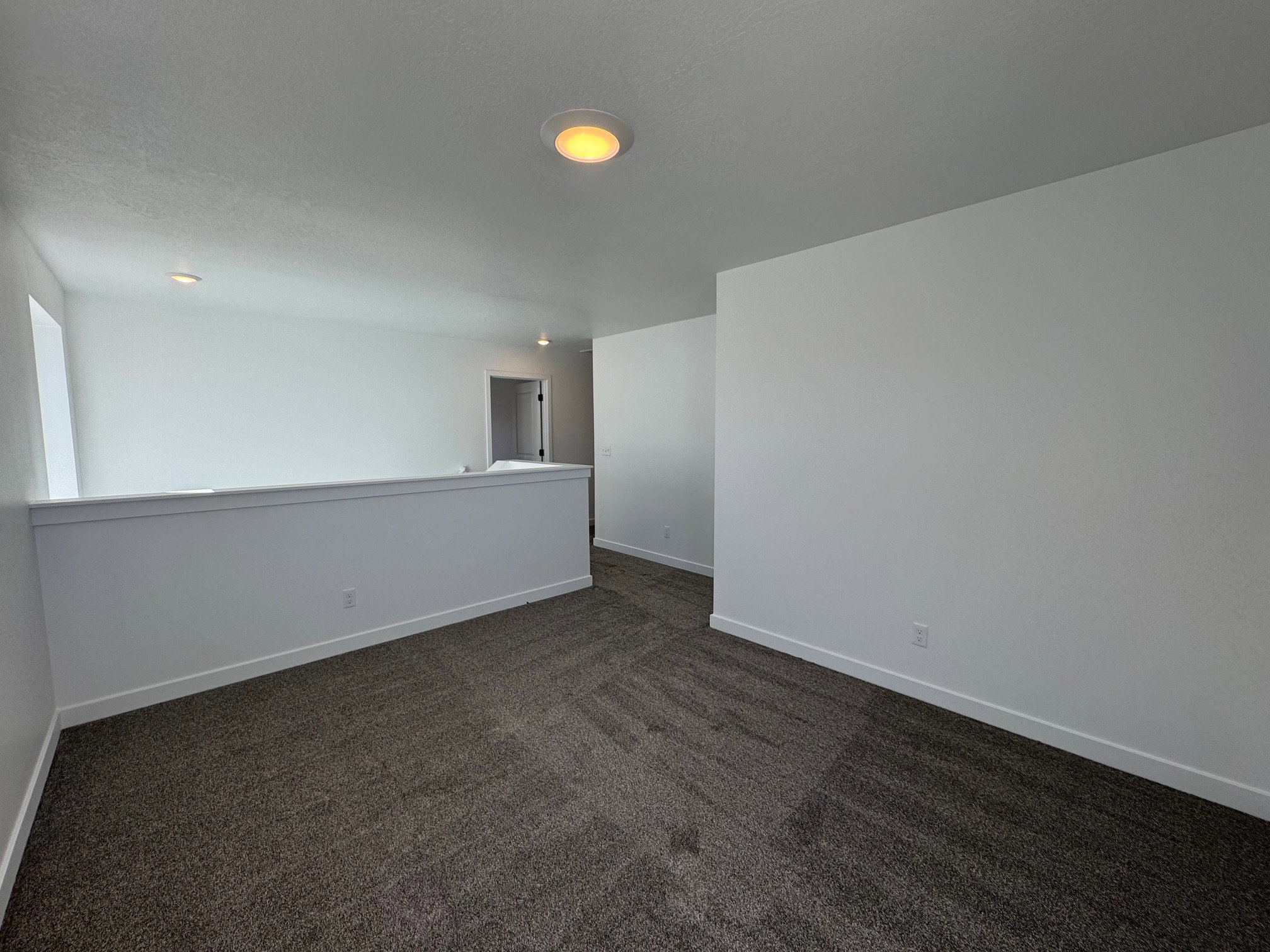 Spacious carpeted landing featuring recessed lighting, a white painted half-wall, and a bright, neutral color palette