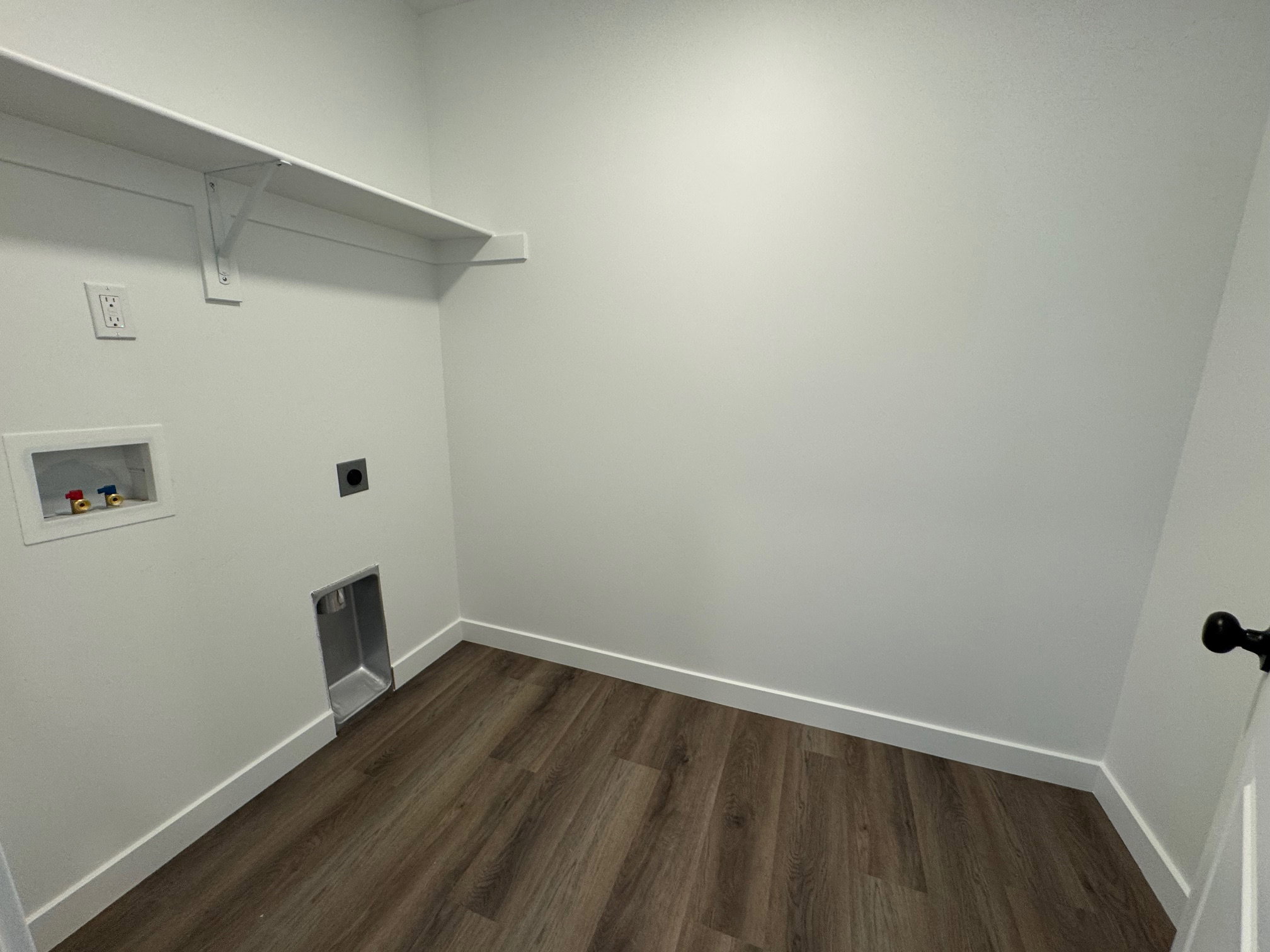 Laundry area featuring wood-finish flooring, white walls, and a white built-in shelf