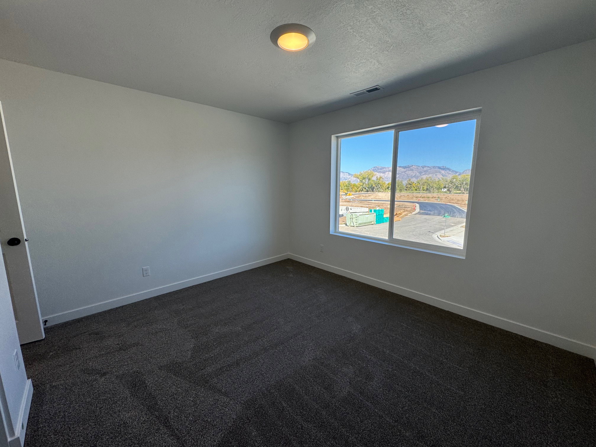 Room featuring a single window, dark gray textured carpeting, white baseboards, and a flush-mount ceiling light