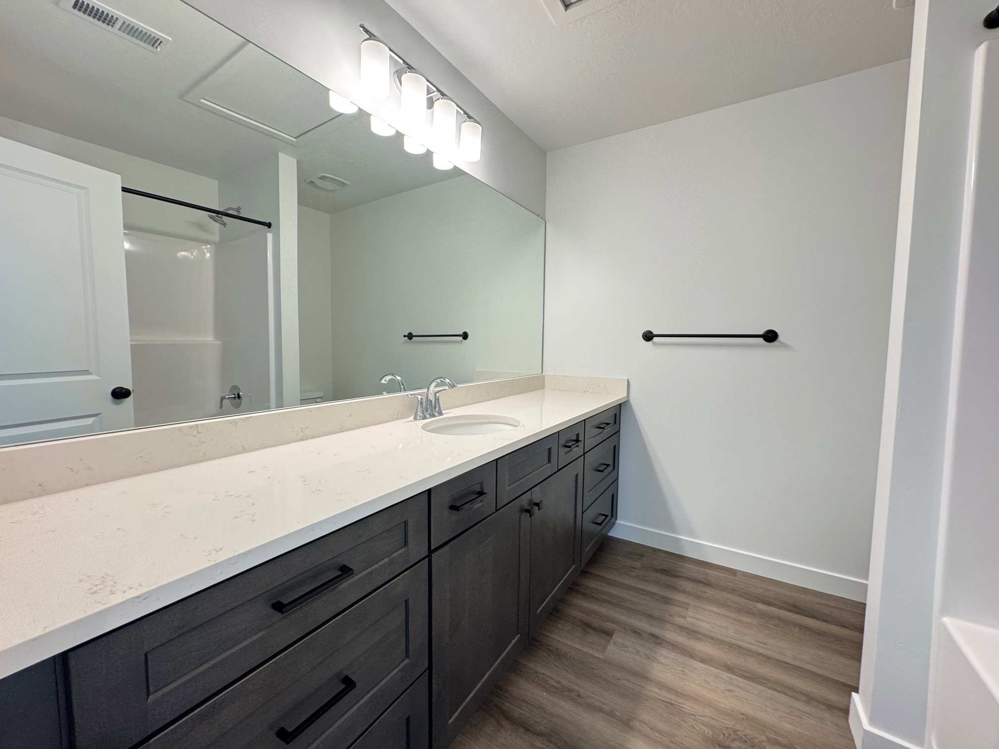 Bathroom featuring a dual-sink vanity with a light-toned countertop, dark wood-finish cabinetry, and wood-finish flooring