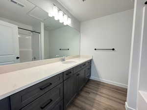 Bathroom featuring a dual-sink vanity with a light-toned countertop, dark wood-finish cabinetry, and wood-finish flooring