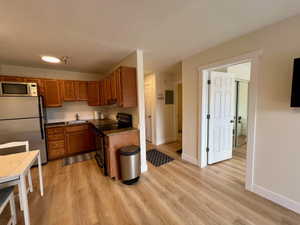 Kitchenette featuring wood-finish flooring, wood cabinetry, granite-look countertops, and stainless steel appliances