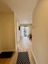 Expansive hallway featuring wood-finish flooring, light neutral wall tones, and white baseboards leading to a balcony with black metal railings