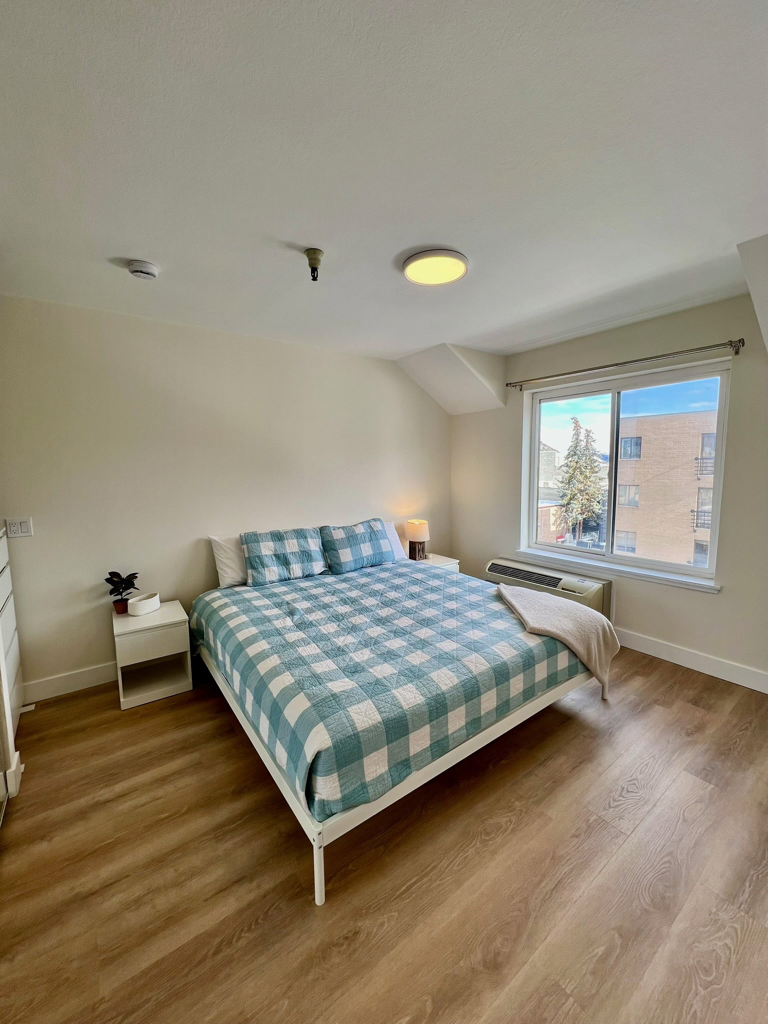 Bedroom featuring wood-finish flooring, a window offering natural light, and an in-wall air conditioning unit
