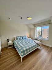 Bedroom featuring wood-finish flooring, a window offering natural light, and an in-wall air conditioning unit