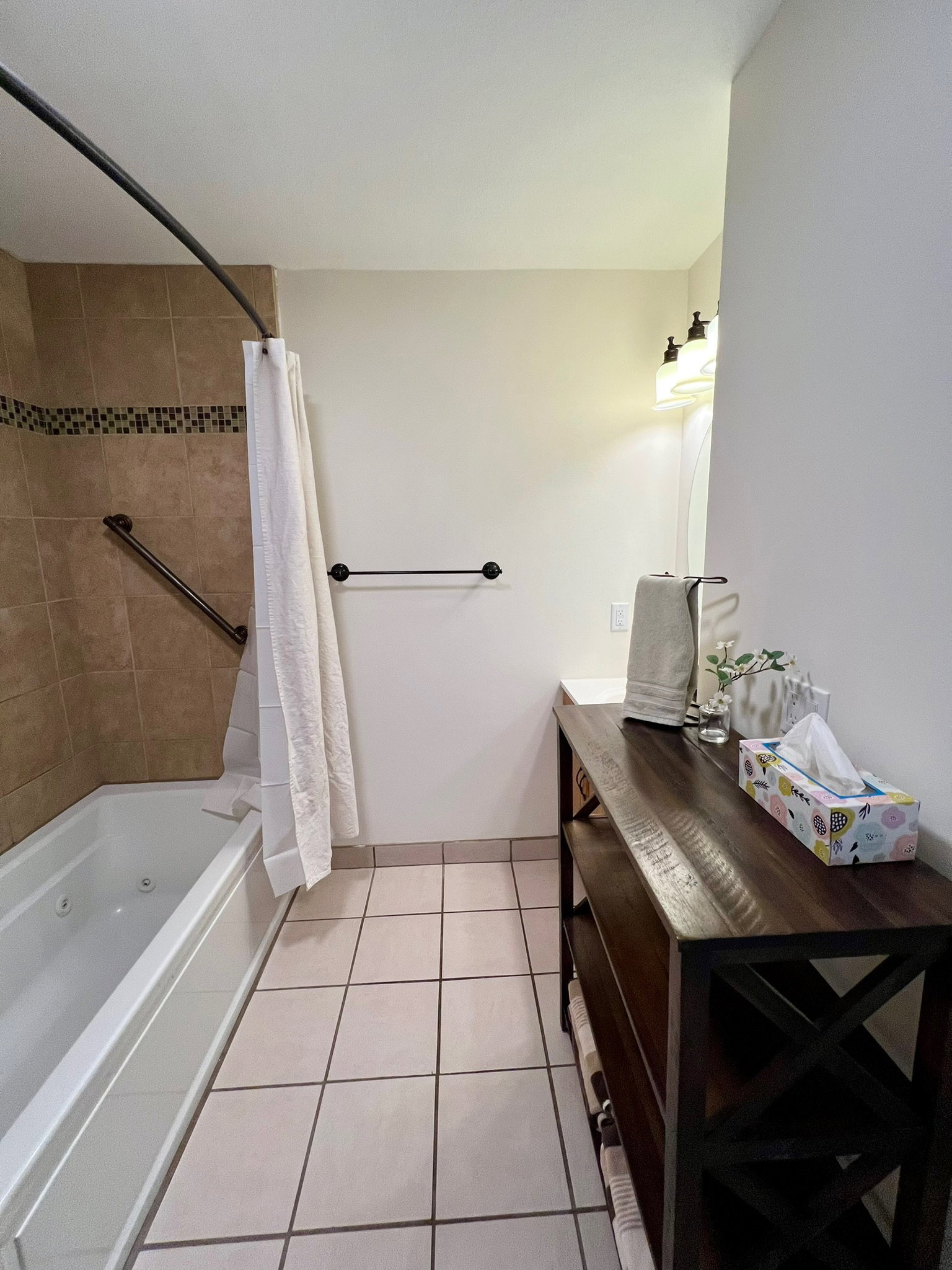 Full bathroom featuring a white soaking tub with jets, tan tile surround with decorative accent band, and a curved shower rod
