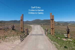 Gated entry to a dirt road, featuring large wooden posts and a rustic wagon wheel accent