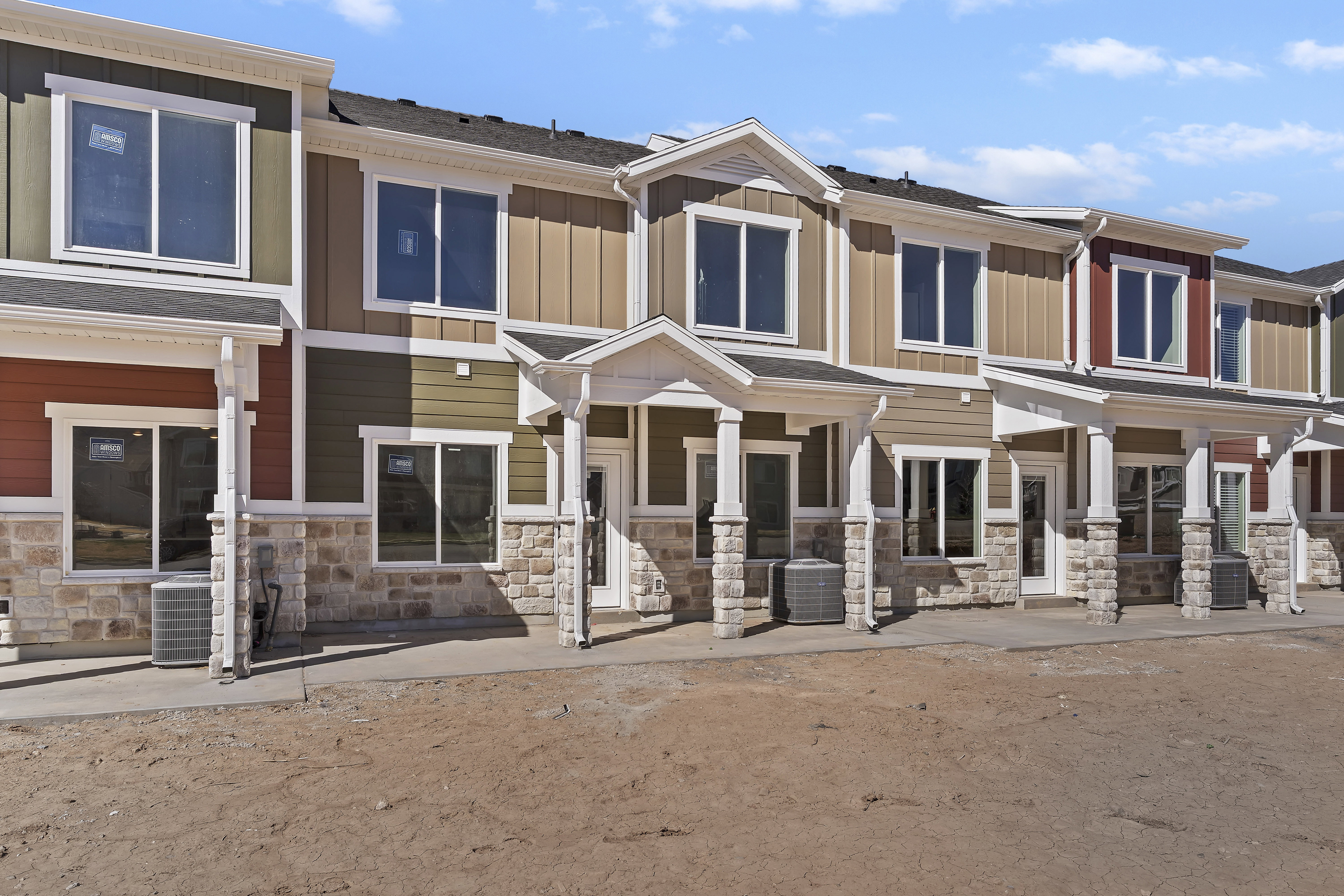 Modern townhome exteriors featuring varied siding colors, stone veneer accents, white trim, and individual covered entryways