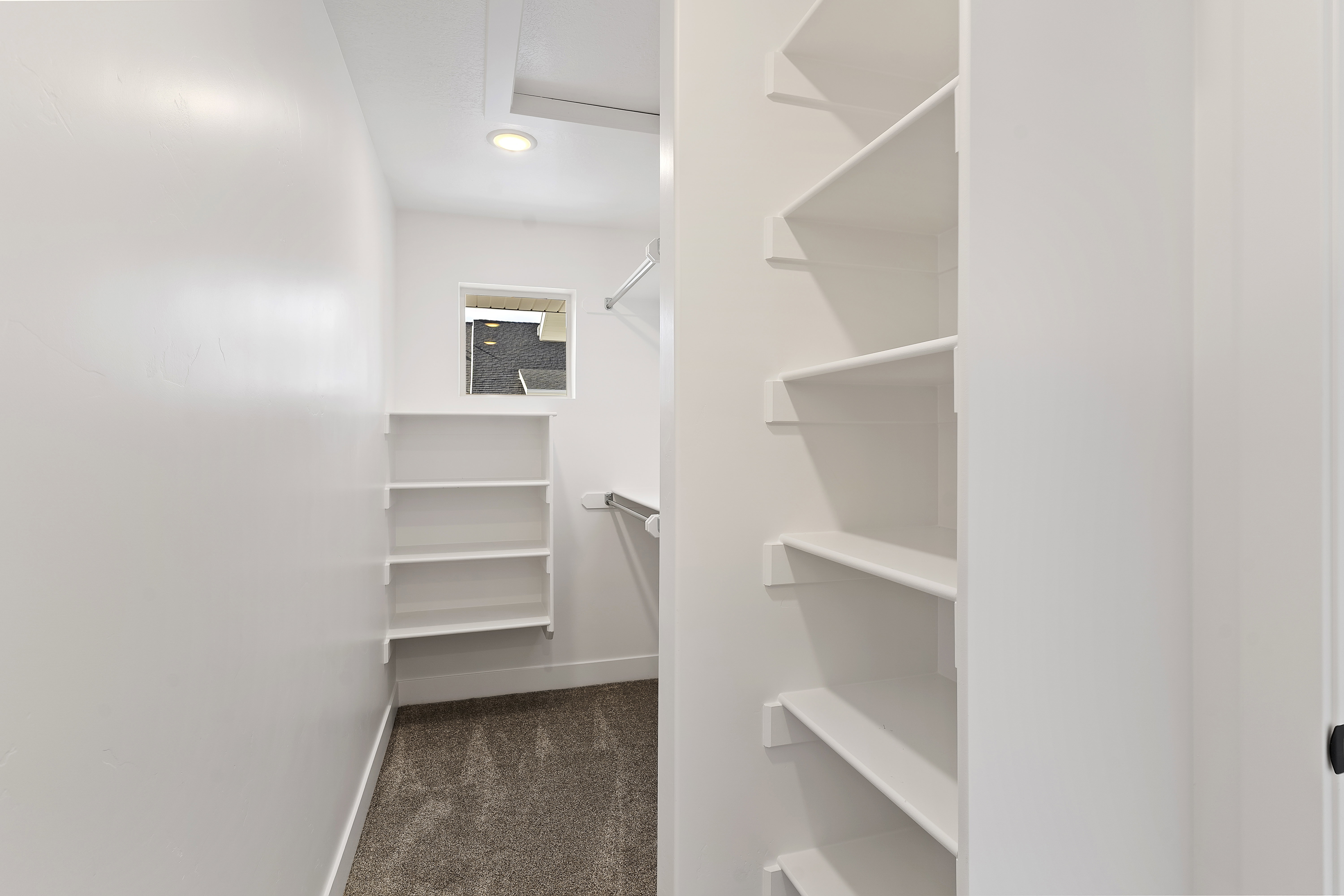 Spacious walk-in closet featuring white built-in shelving, hanging rods, and recessed lighting