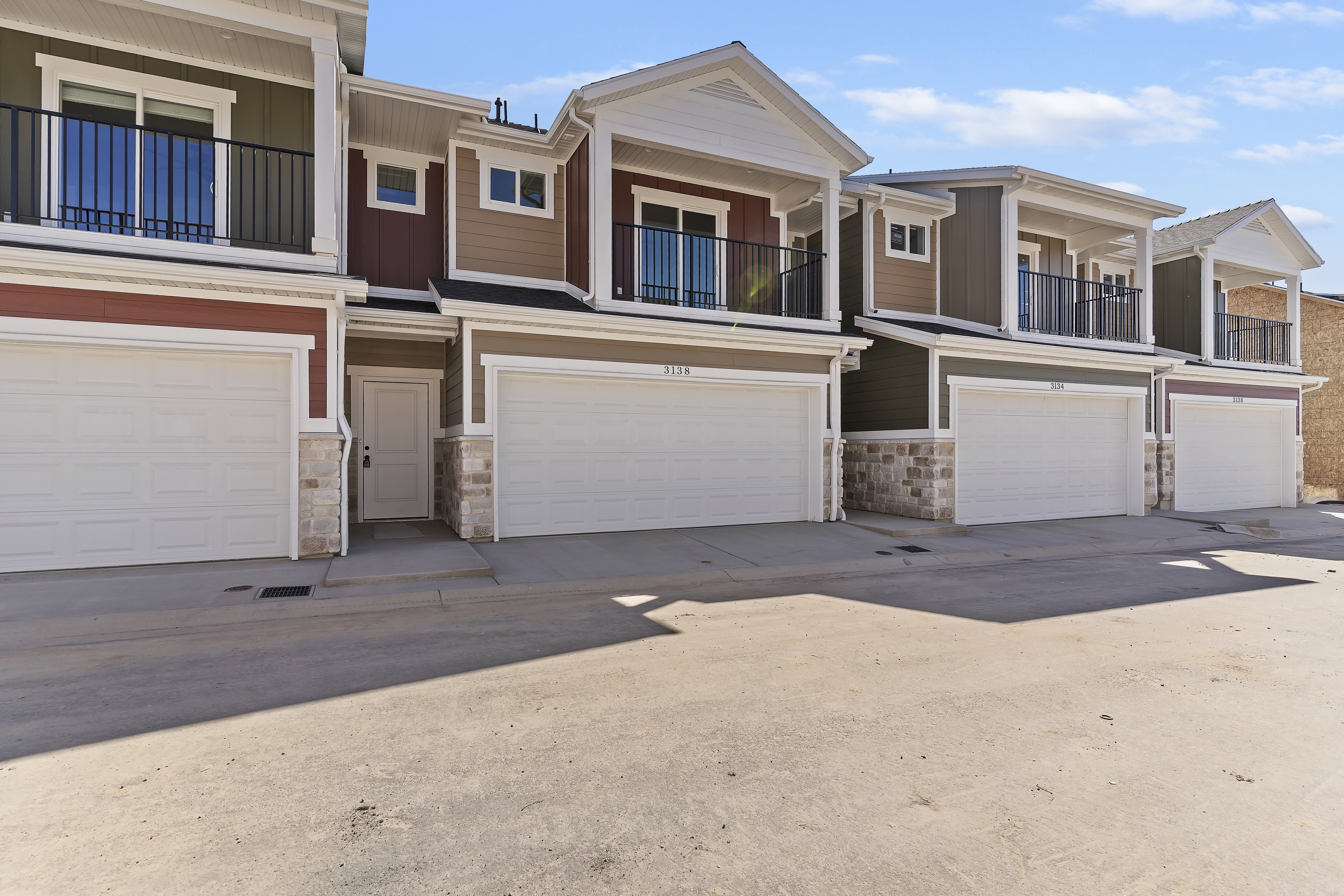 Contemporary townhome exterior featuring multi-toned siding, stone accents, and a covered balcony with black railings