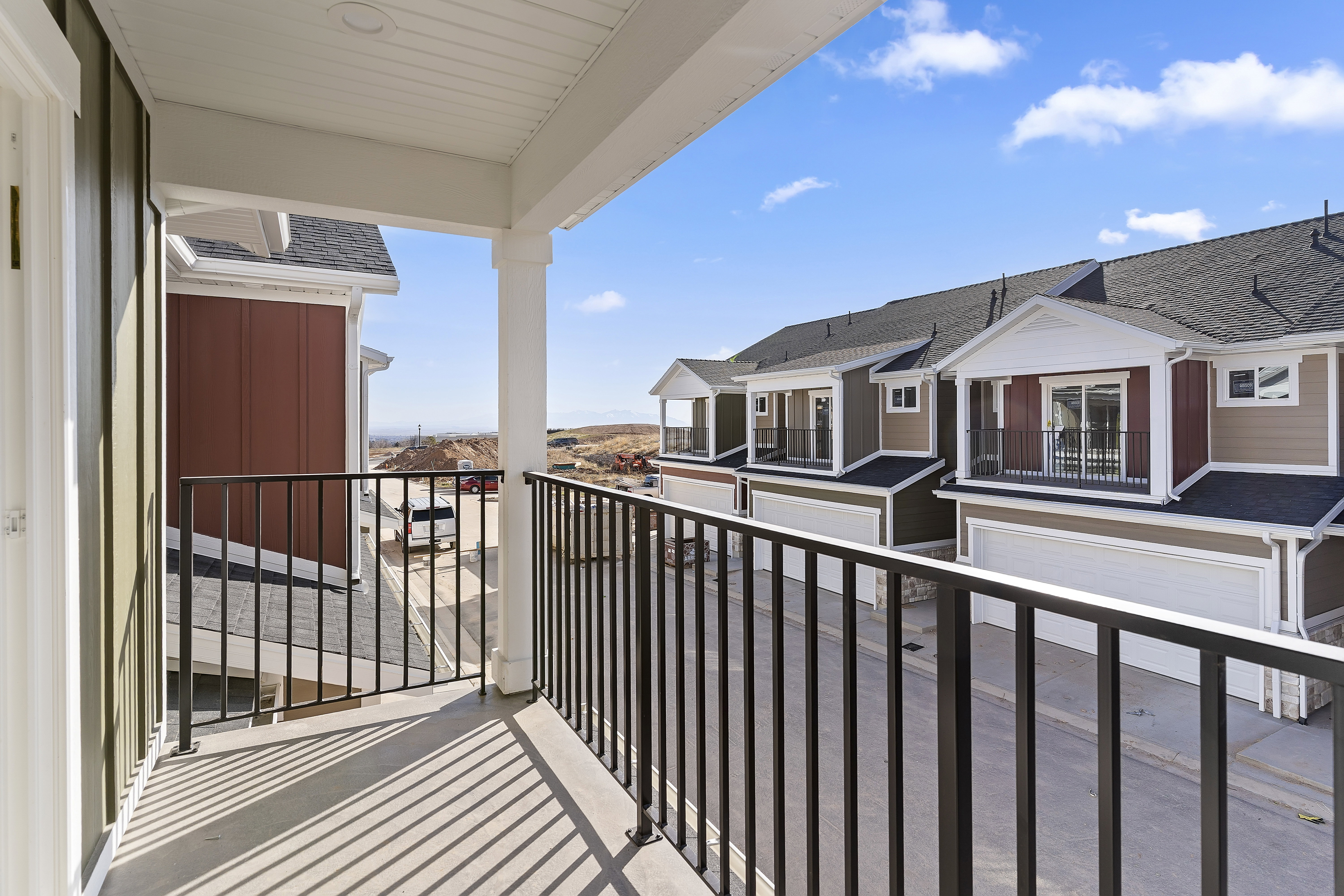 Private balcony with black metal railing, offering exterior views of the residential street and distant terrain