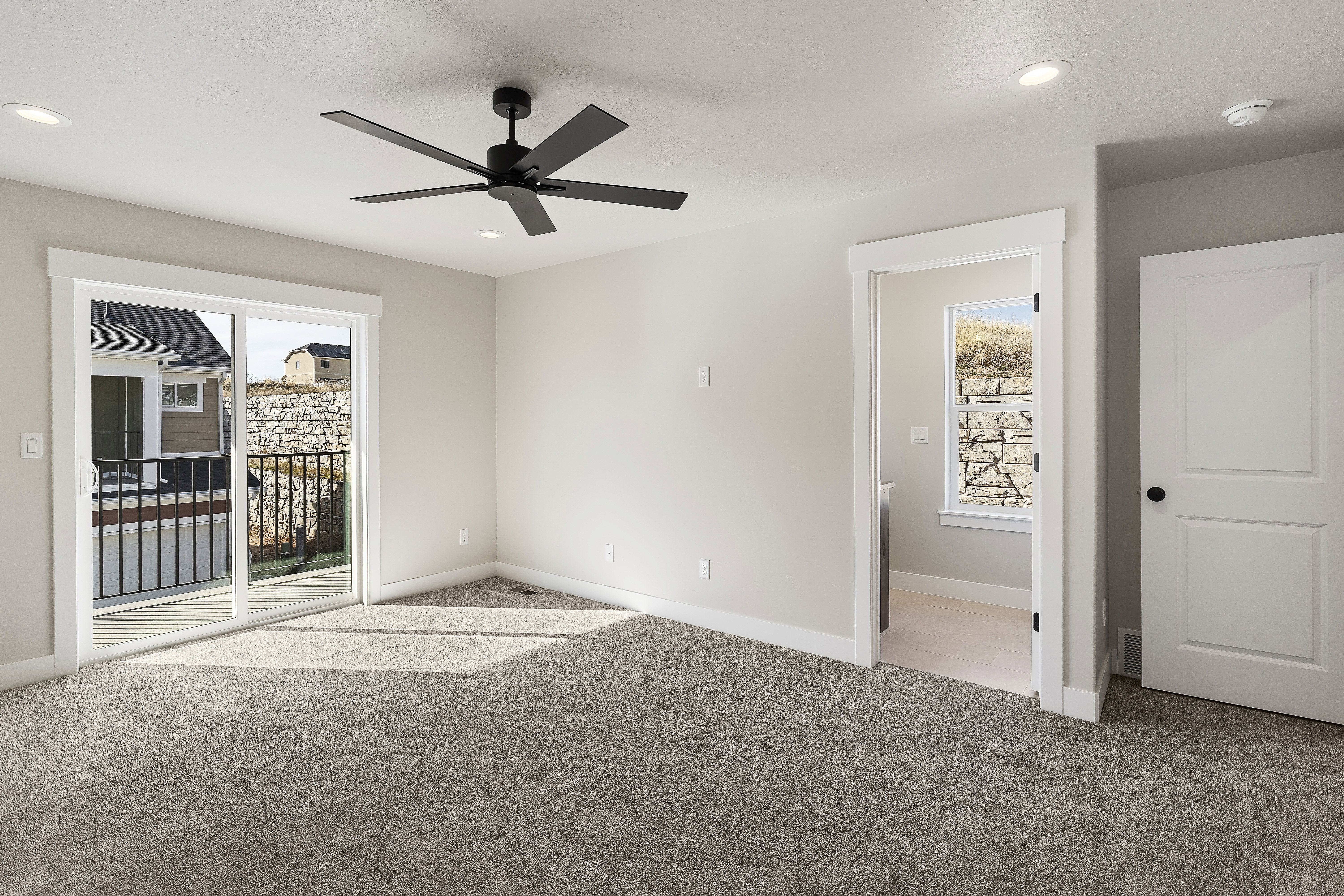 Carpeted room with a sliding glass door leading to an outdoor balcony with black railings