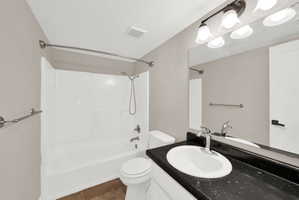 Bathroom featuring a white tub/shower combination, dark speckled countertop, and a vanity light fixture with frosted glass shades