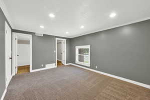 Spacious room with gray walls and neutral-toned carpeting, featuring recessed lighting, a single window, white trim, and two doorways