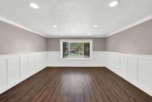Spacious room featuring rich wood-finish flooring, crisp white wainscoting, and crown molding