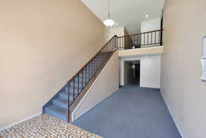 Two-story entryway featuring a carpeted staircase with wood and metal railings, light beige painted walls, and an overhead pendant light fixture