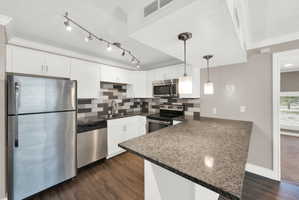Kitchen featuring white cabinetry, stainless steel appliances, a grey and white tile backsplash, wood-finish flooring, and a stone countertop with a breakfast bar