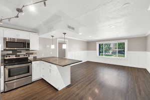 Open-concept kitchen and living area featuring wood-finish flooring, white cabinetry, stainless steel appliances, and a granite-look island countertop