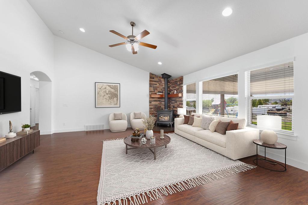 Spacious living area featuring wood-finish flooring, vaulted ceilings, and a corner wood-burning stove with a stone surround