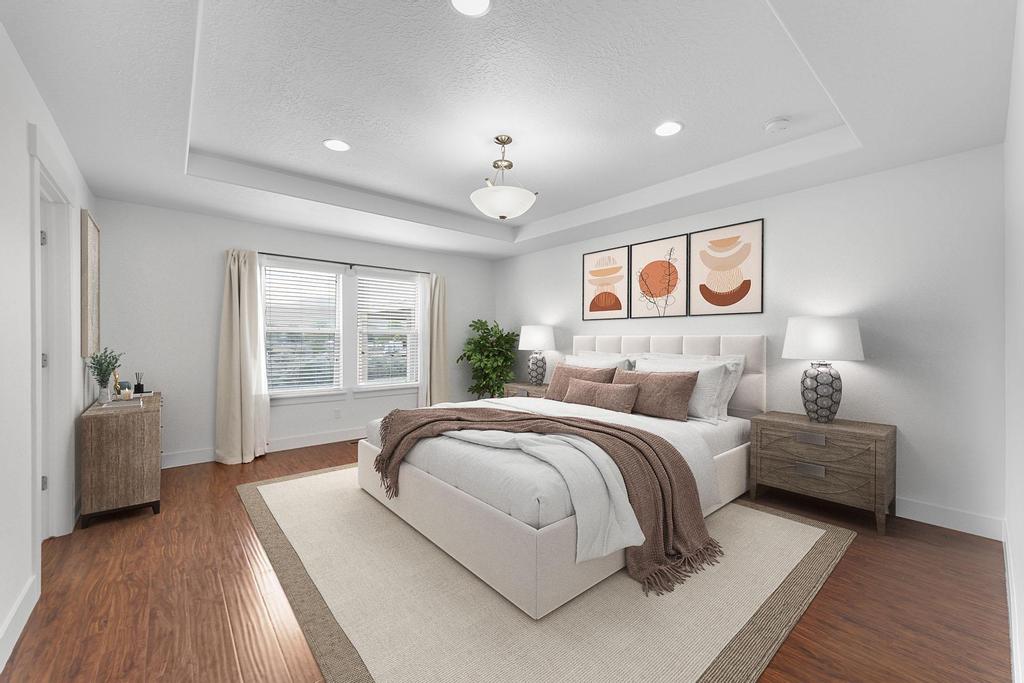 Recessed lighting illuminates a tray ceiling and wood-finish flooring