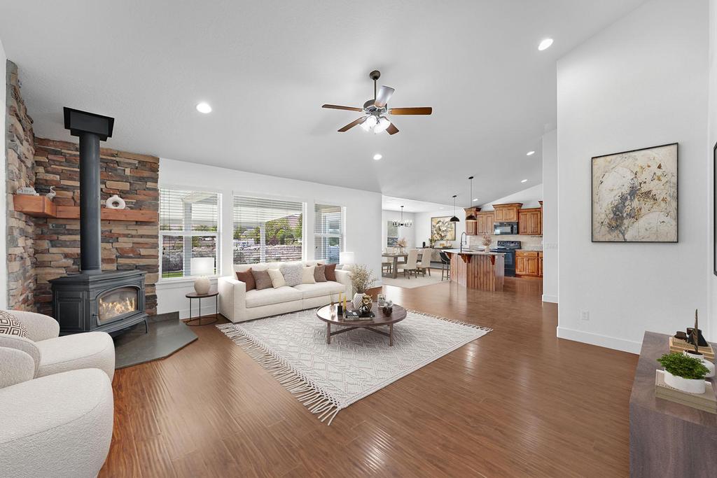 Spacious living area featuring wood-finish flooring, a stone accent wall with a wood-burning stove, large windows, and recessed lighting