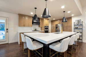 Gourmet kitchen featuring a large central island with seating, stone countertops, wood-finish flooring, recessed lighting, and a gold-tone faucet