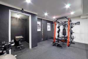 Dedicated fitness area featuring durable rubber flooring, dark textured wall finishes, recessed lighting, and a white ceiling