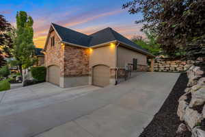 Multi-level home exterior featuring stone and stucco finishes, a dark shingle roof, and multiple garage doors