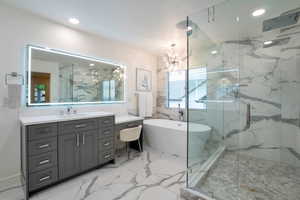 Contemporary bathroom featuring a freestanding soaking tub, a spacious glass-enclosed shower, a large vanity with integrated lighting, a quartz countertop, and large-format porcelain tile flooring