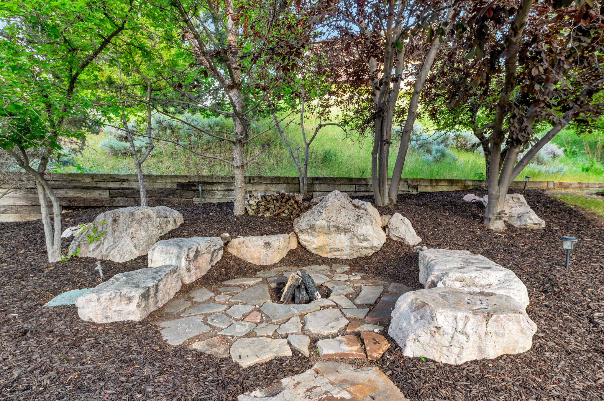 Gather around the custom stone fire pit nestled beneath mature trees—an inviting space for relaxing evenings and entertaining family and friends.