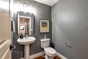 Powder room featuring a pedestal sink, white baseboards, a wall-mounted mirror with a black frame, and wood-finish flooring