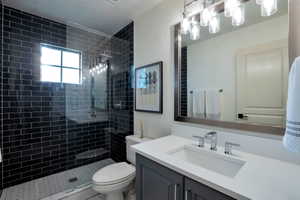 Bathroom featuring a frameless glass shower enclosure with dark subway tile, a white vanity with an integrated sink, a rectangular framed mirror, and a contemporary multi-bulb light fixture