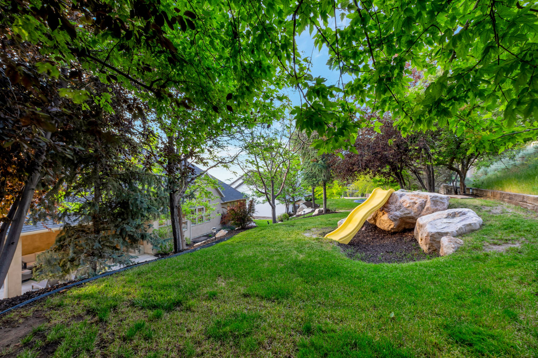 Large, shaded backyard with mature trees, established landscaping, and plenty of space to enjoy Utah's beautiful seasons.
