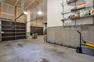 Two brown garage doors, concrete flooring, exposed wood framing, concrete foundation wall, and wall-mounted wire shelving
