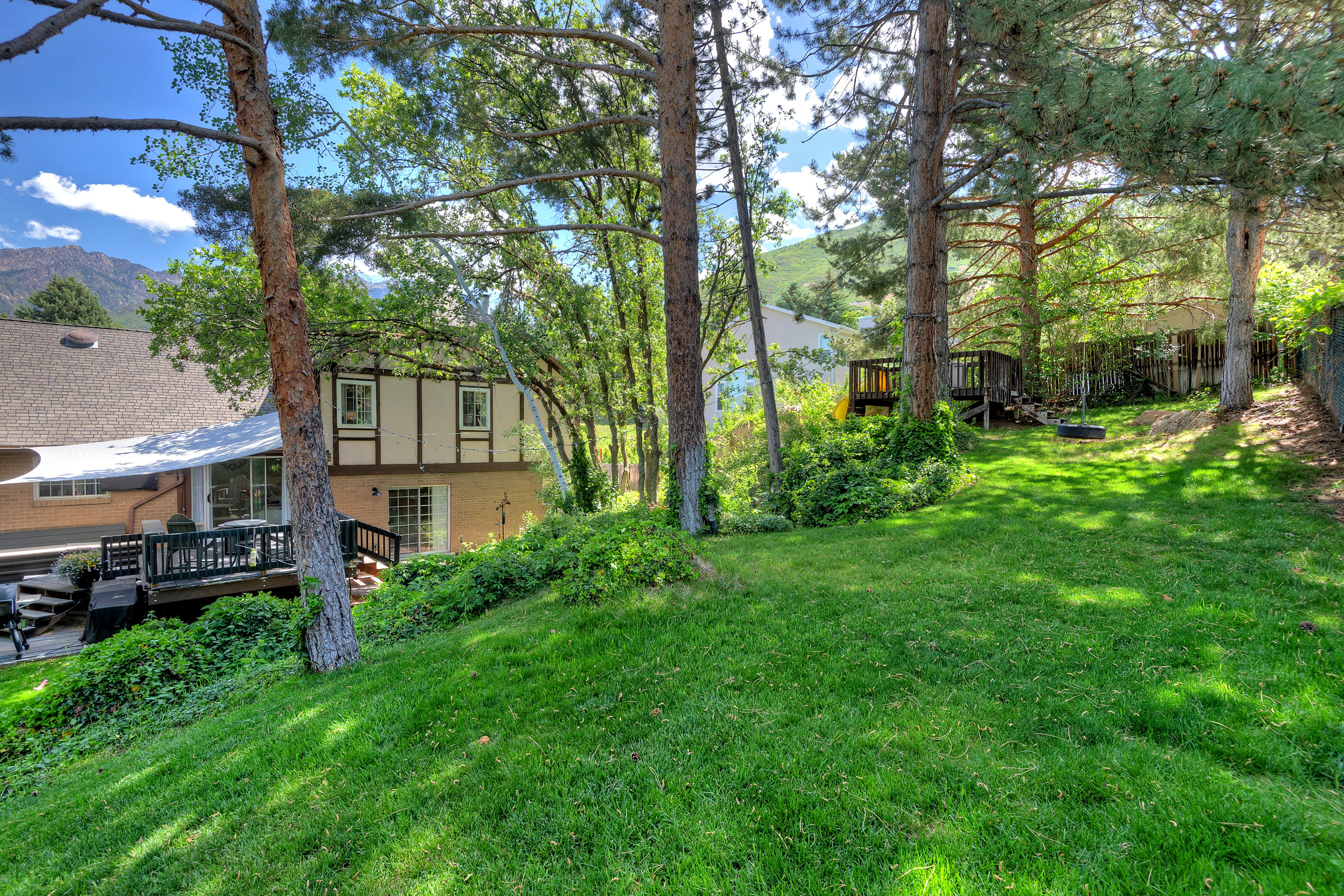 Sloping grassy yard with mature trees and a mountain backdrop
