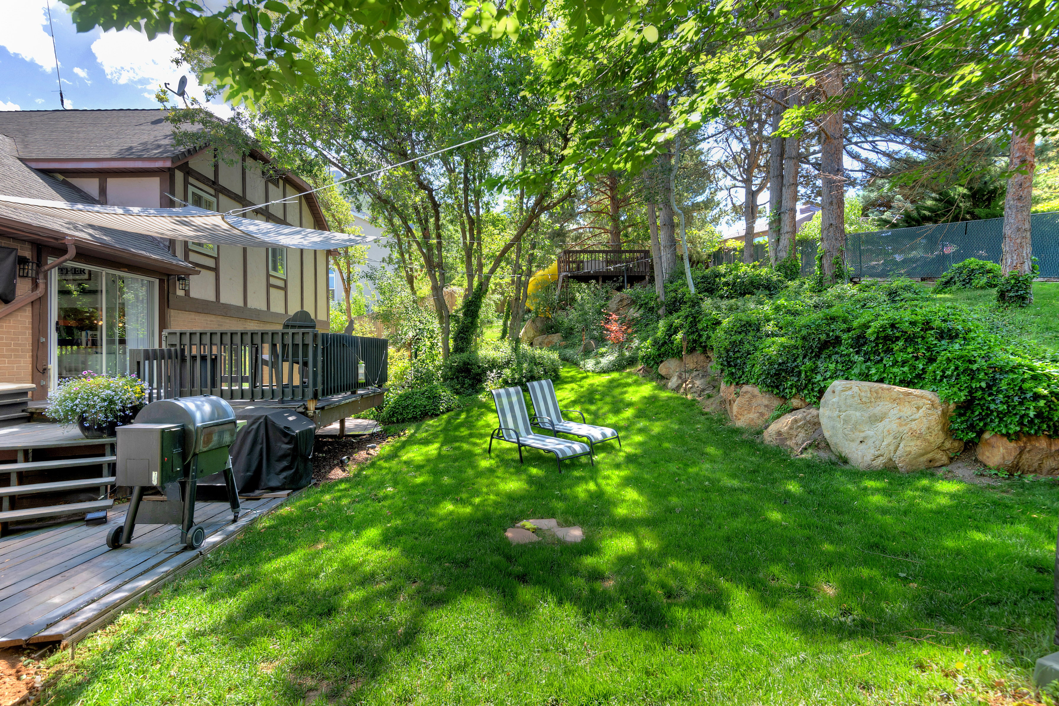 Expansive backyard featuring a manicured lawn, established trees, and a multi-level wood deck