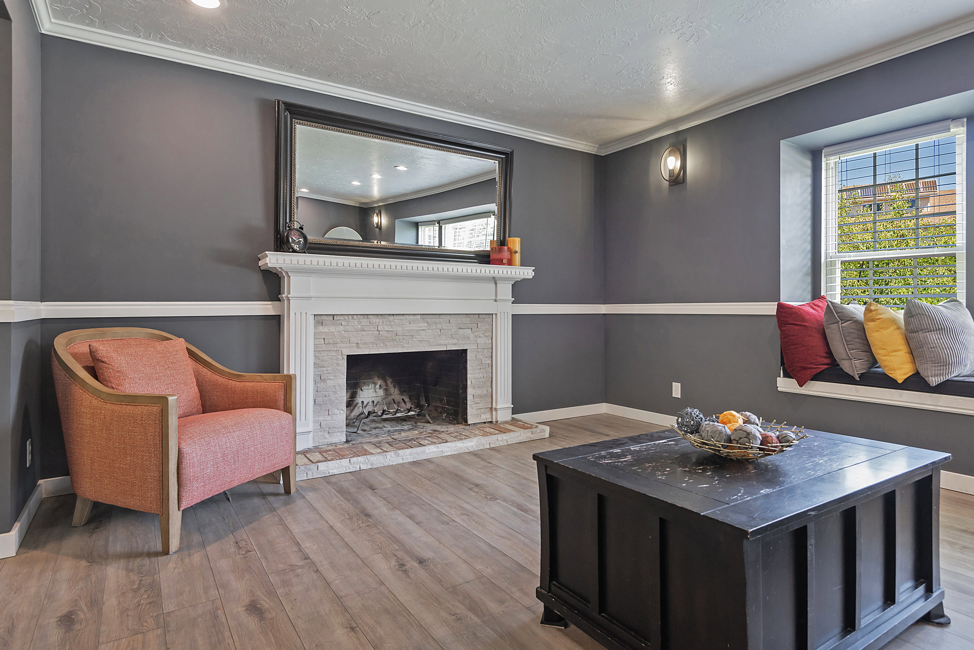 Living area featuring a white mantel fireplace with a stacked stone surround and brick hearth, a built-in window seat, wood-finish flooring, recessed lighting, and wall sconces