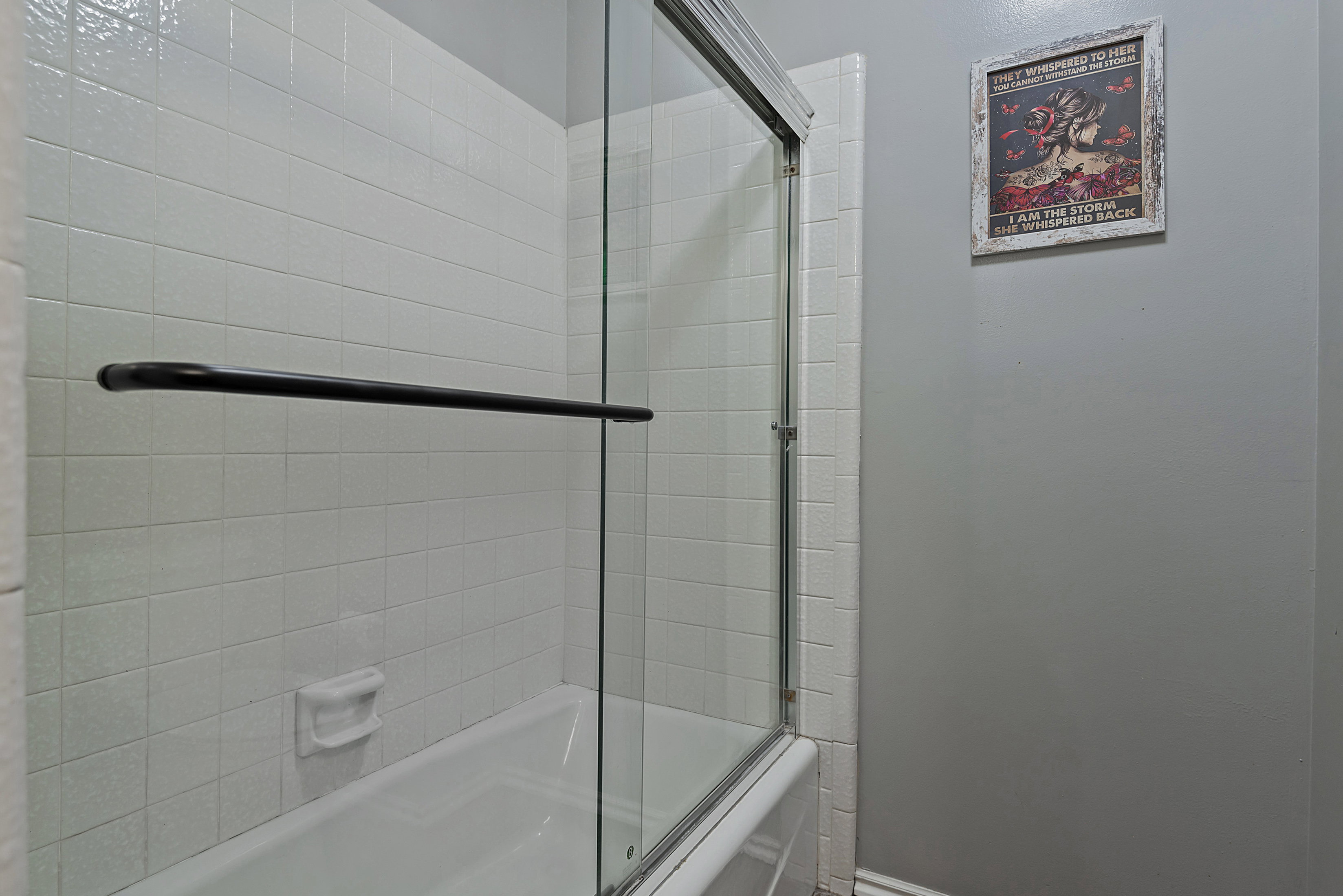 Bathtub with white tile surround and clear glass sliding shower doors
